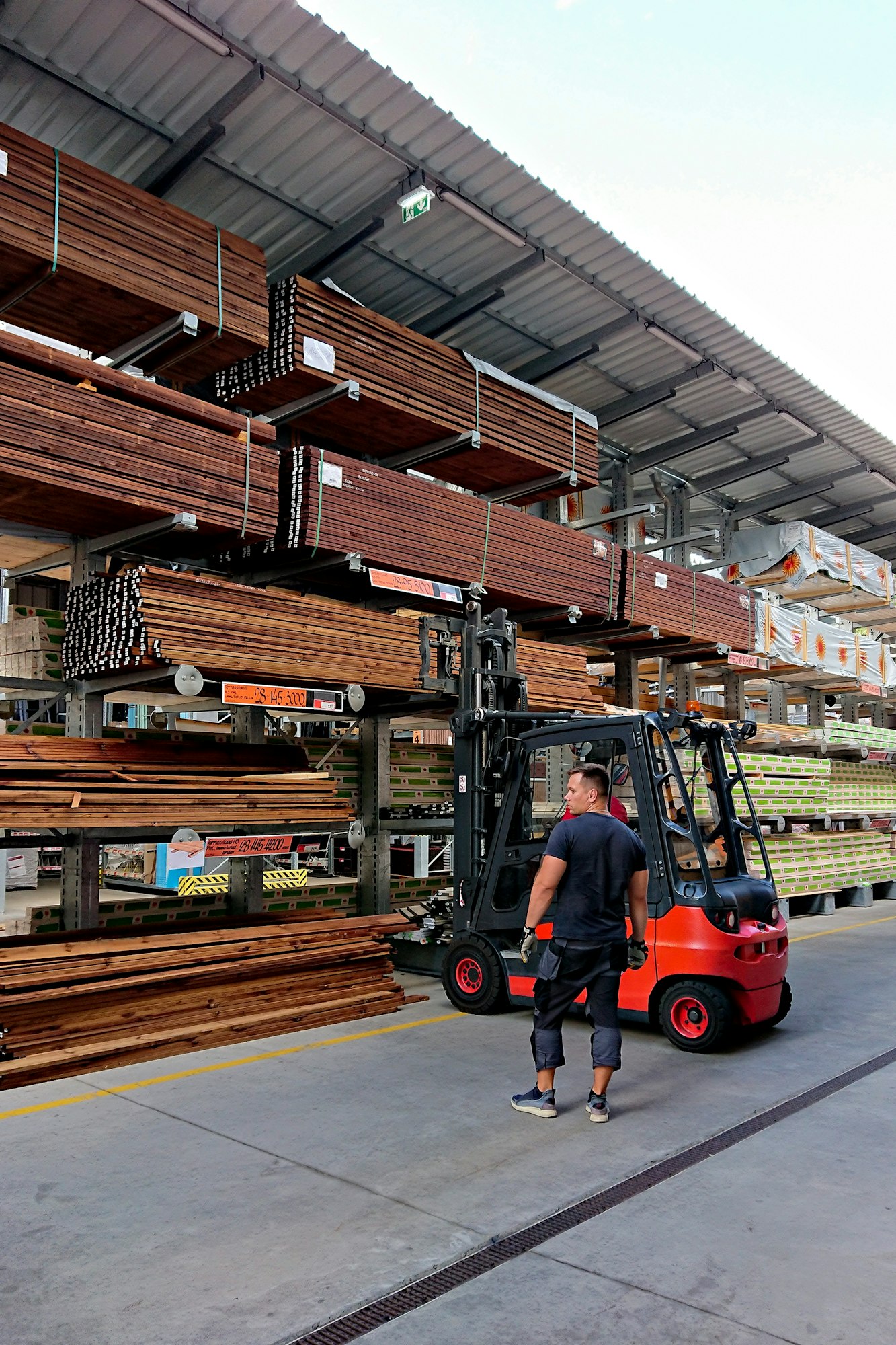 Working guy working in open-air warehouse of building materials and electric powered rider truck